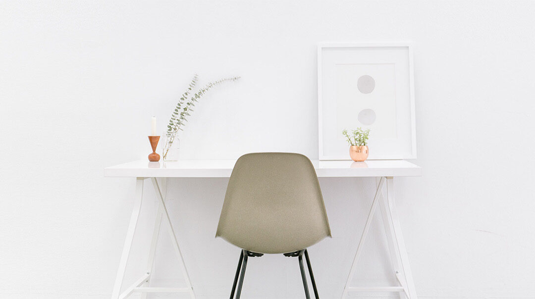 Minimalist white desk with plant and print and chair up against a white wall