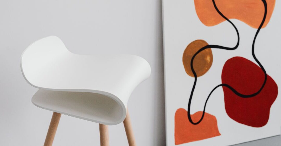 unique white chair with three wooden legs next to an abstract painting of shades of orange and red blobs