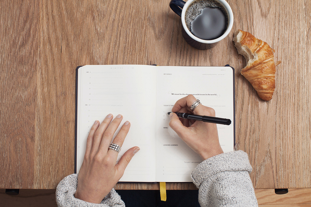 woman writing in a planner with coffee and a croissant sitting next to her. This is a way to help if you're suffering from analysis paralysis