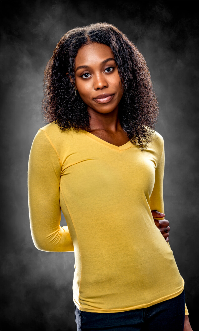 Portrait of an African American woman posing with a yellow long-sleeved shirt with her arms behind her back