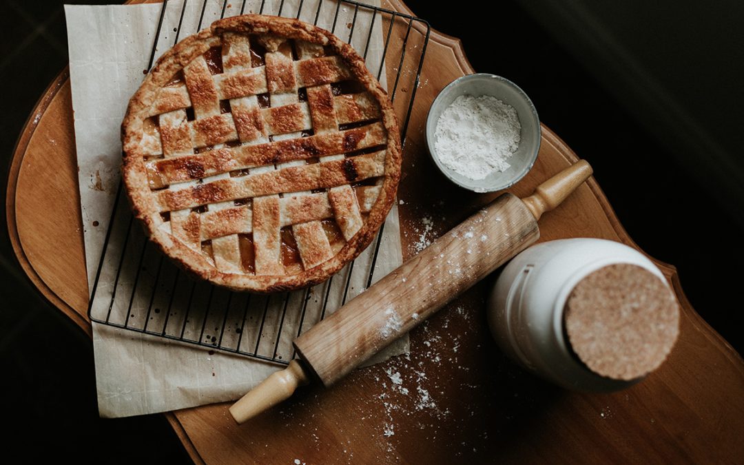 fresh baked apple pie with a rolling pin and some flour dust on a table
