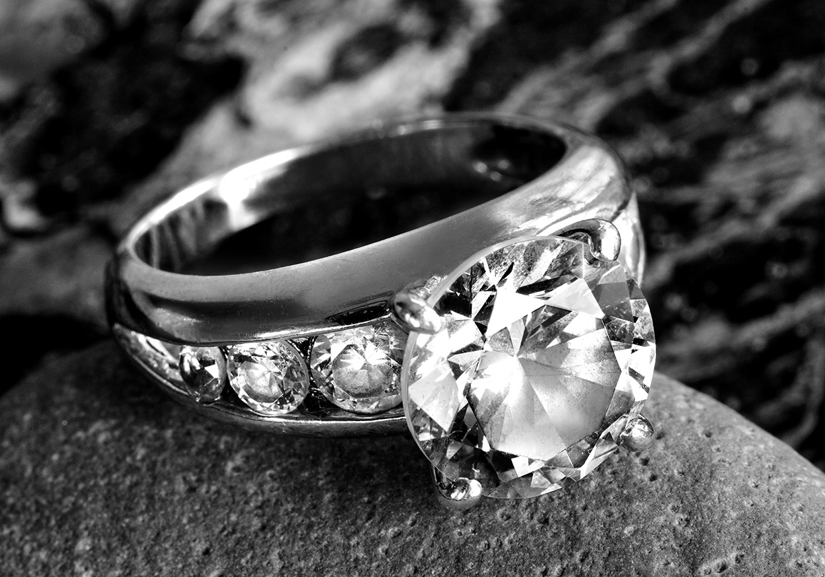diamond wedding ring with large circular diamond and smaller diamonds inset. black and white.