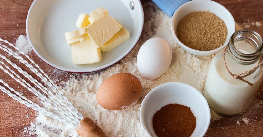 ingredients for baking on a wood table butter eggs sugar milk vanilla flour and a whisk