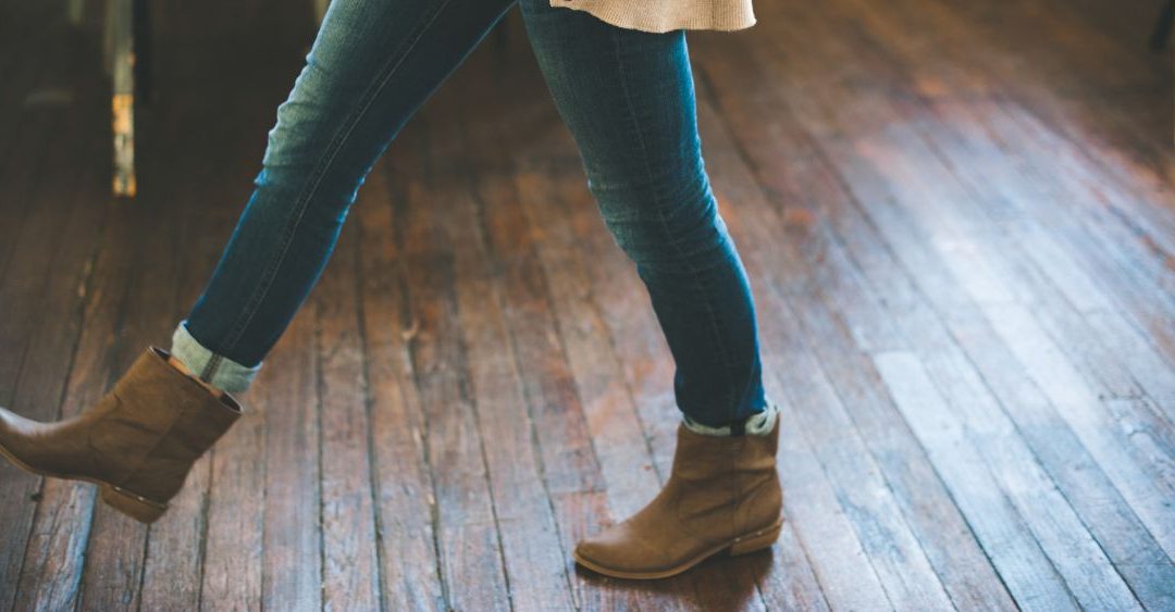 closeup of a woman wearing a cardigan, jeans, and ankle boots taking a step on wood floor