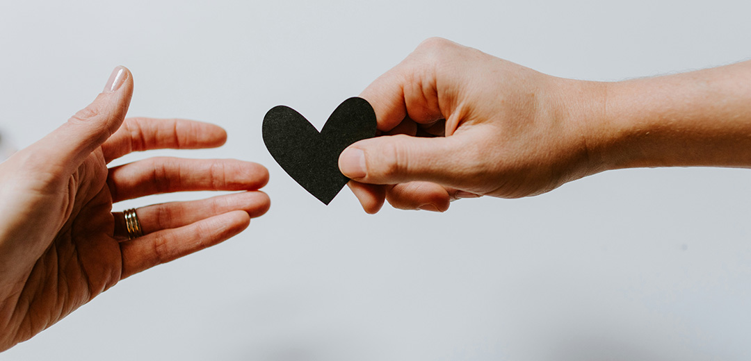 hand holding out a black paper heart for another hand to grab